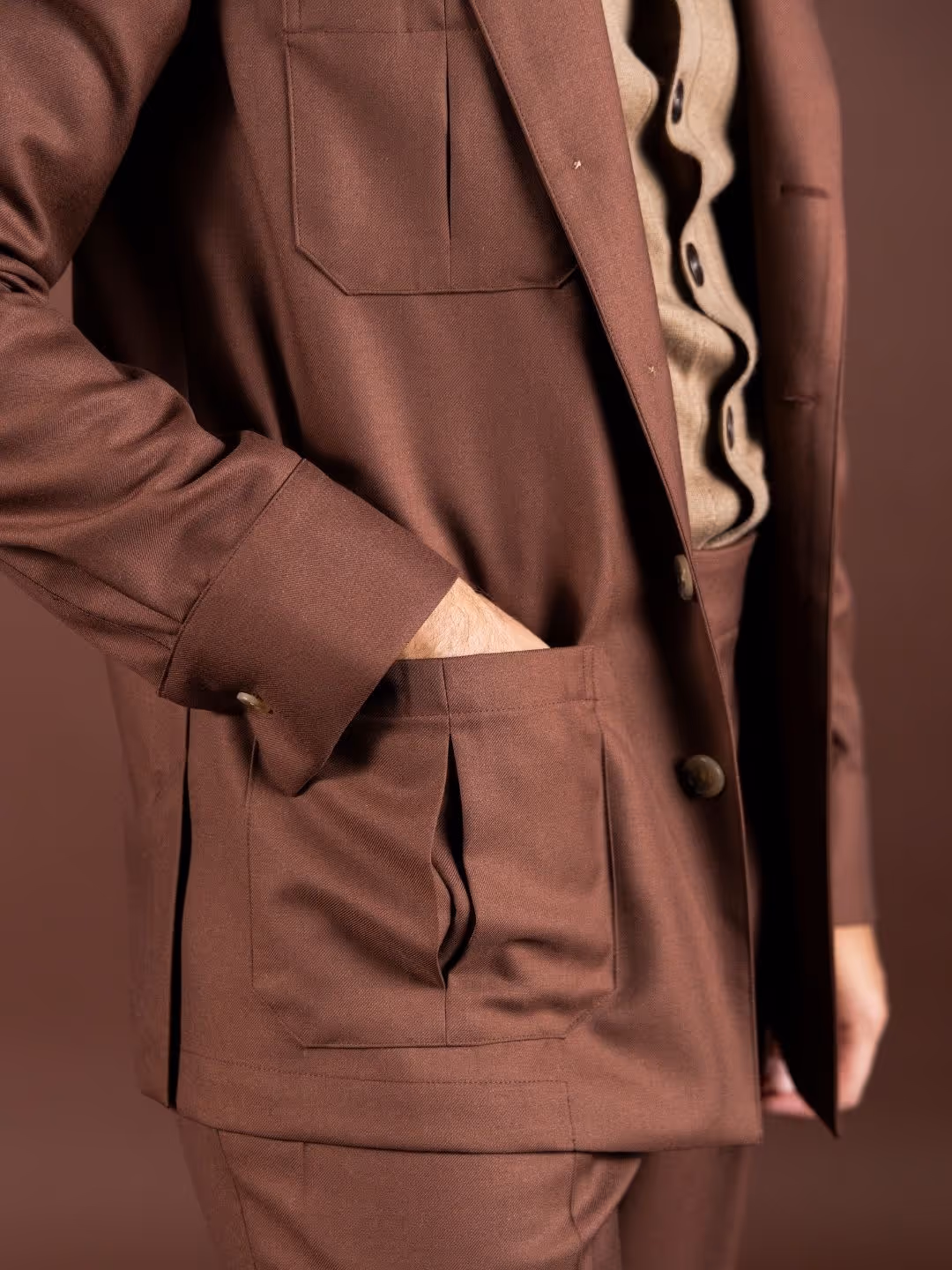 Nahaufnahme einer Person in braunem Anzug mit Hand in der Hosentasche vor braunem Hintergrund.