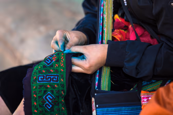 Close-up of a woman hand-dyeing and embroidering traditional fabric with indigo patterns in Sapa.