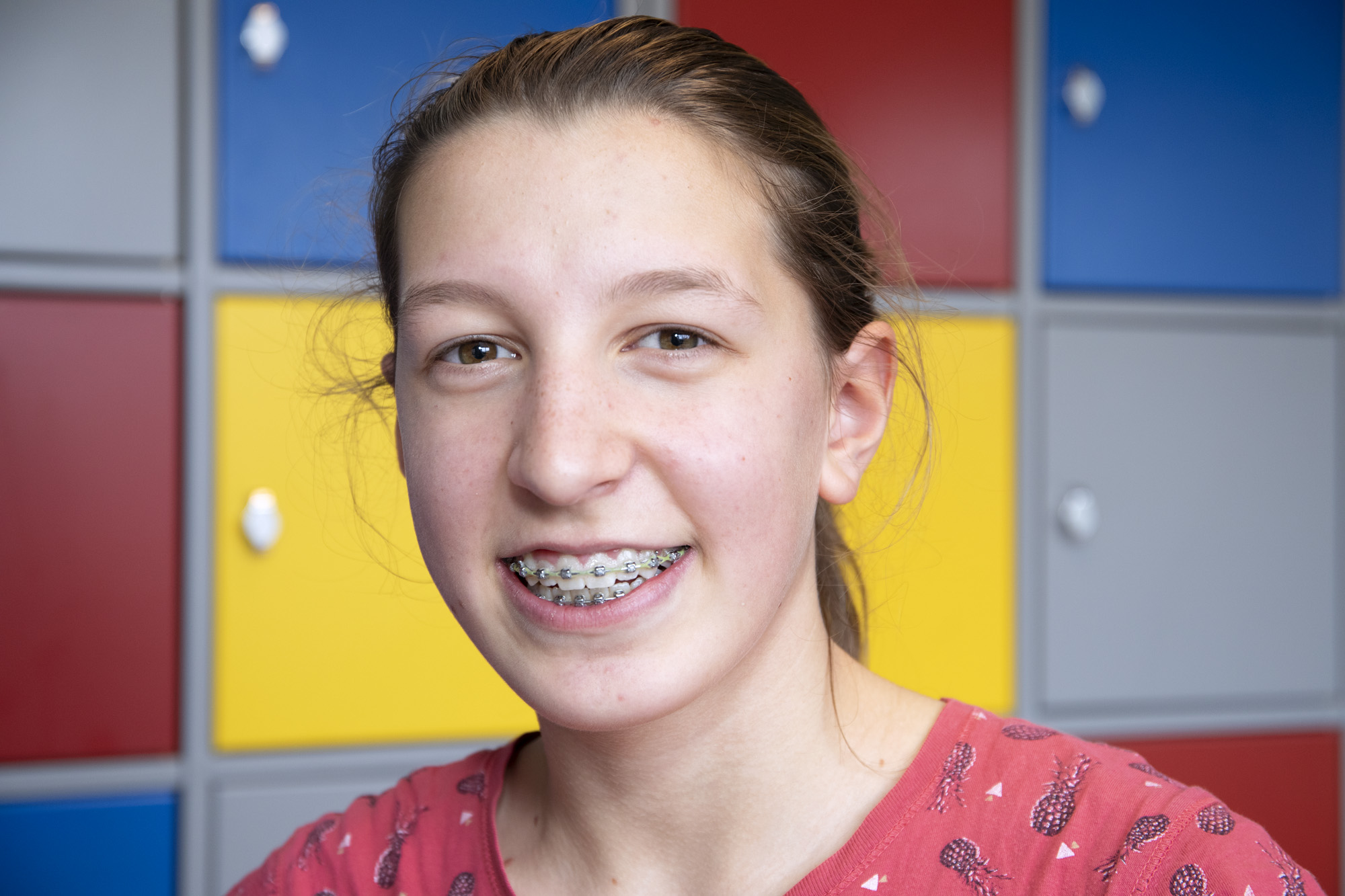 Portret foto van een jonge, lachende MDT deelnemer voor een muur met schoolkluisjes 