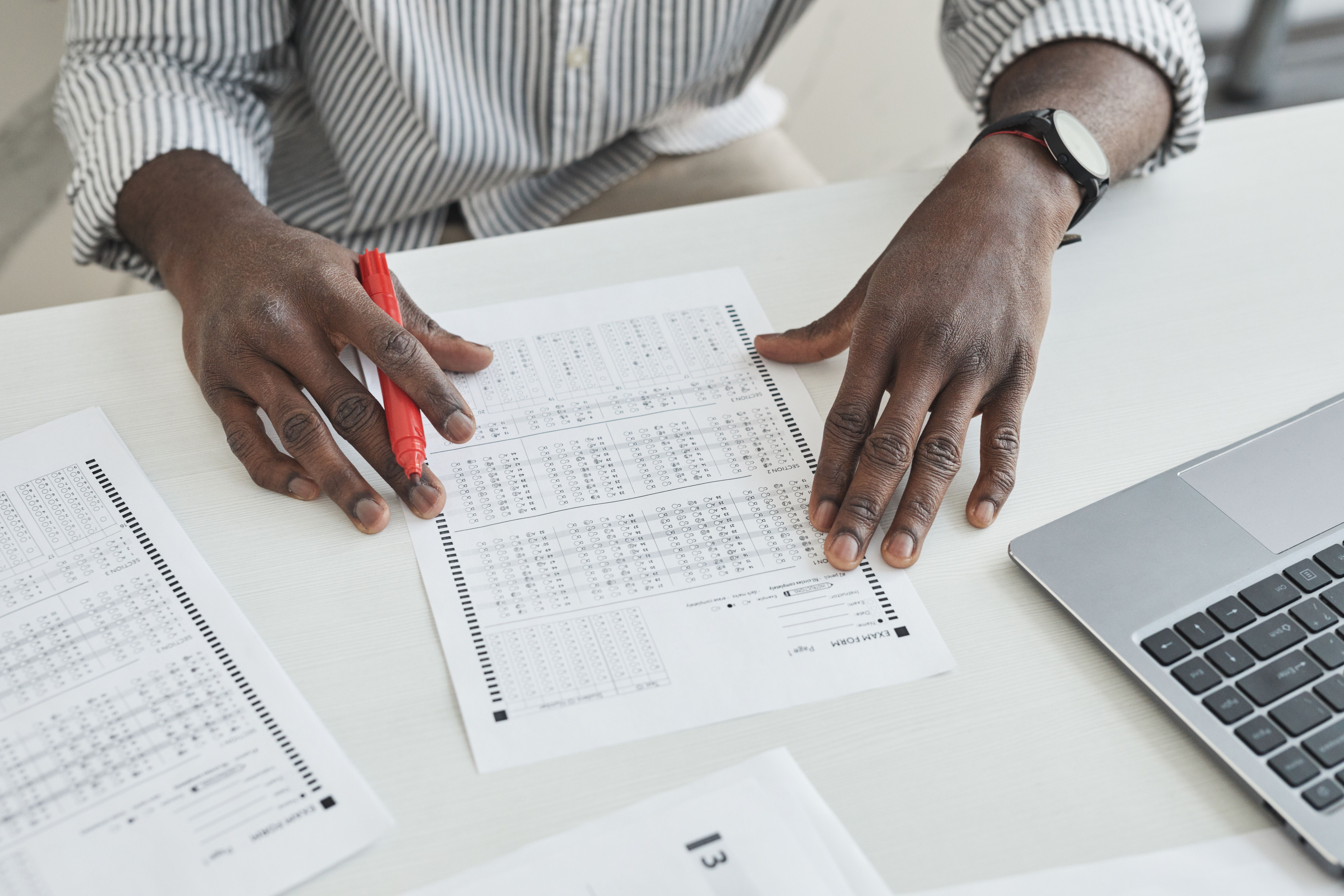 Teacher marking exam papers with a red pen at a desk