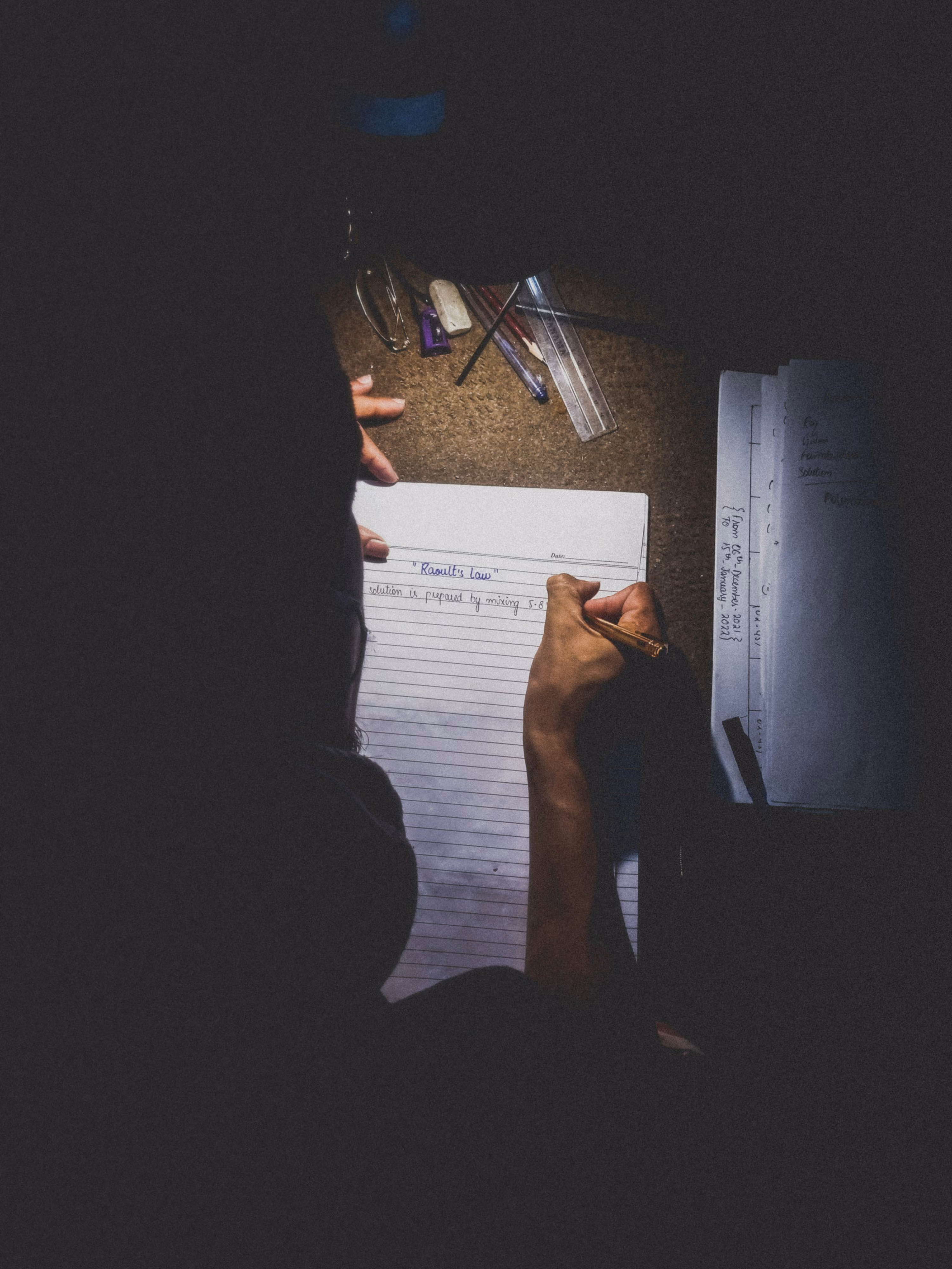 A student studying at a desk at night, focused on completing written work