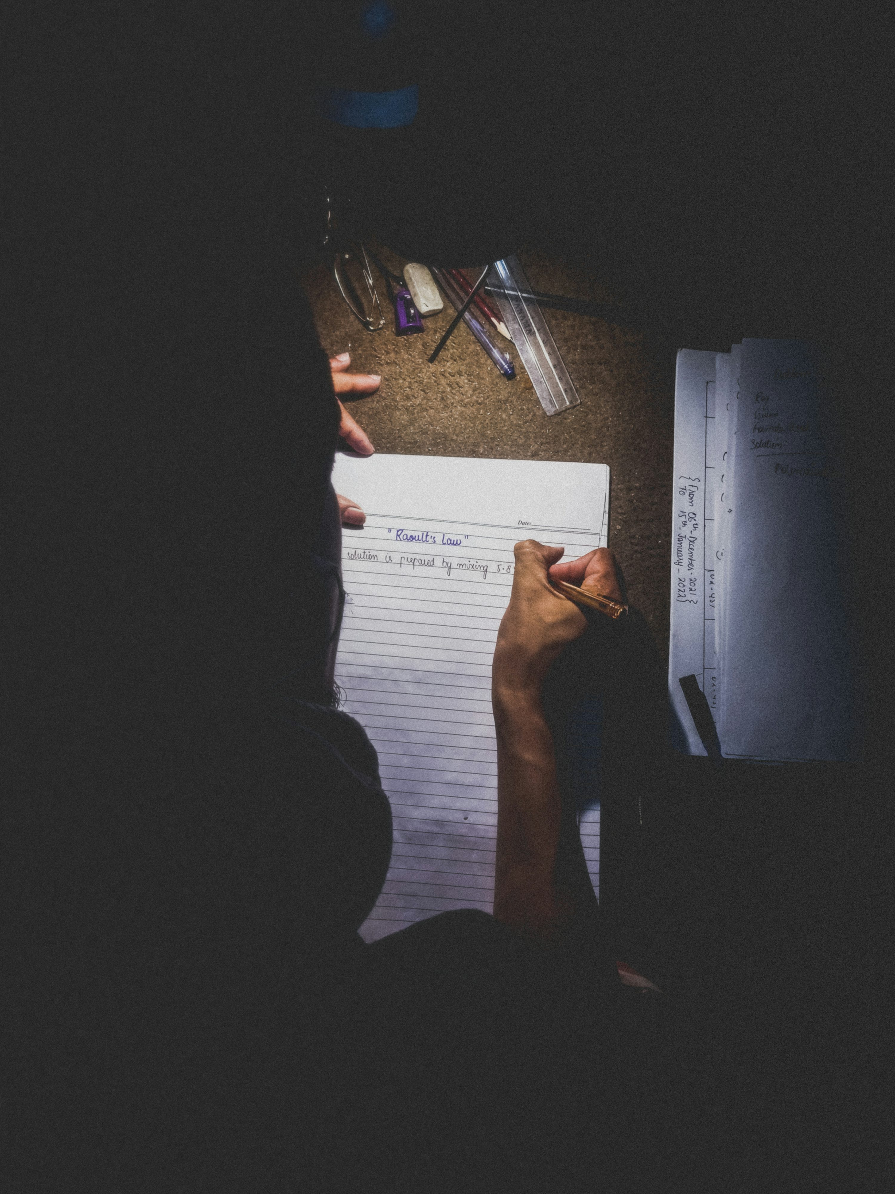 A student studying at a desk at night, focused on completing written work