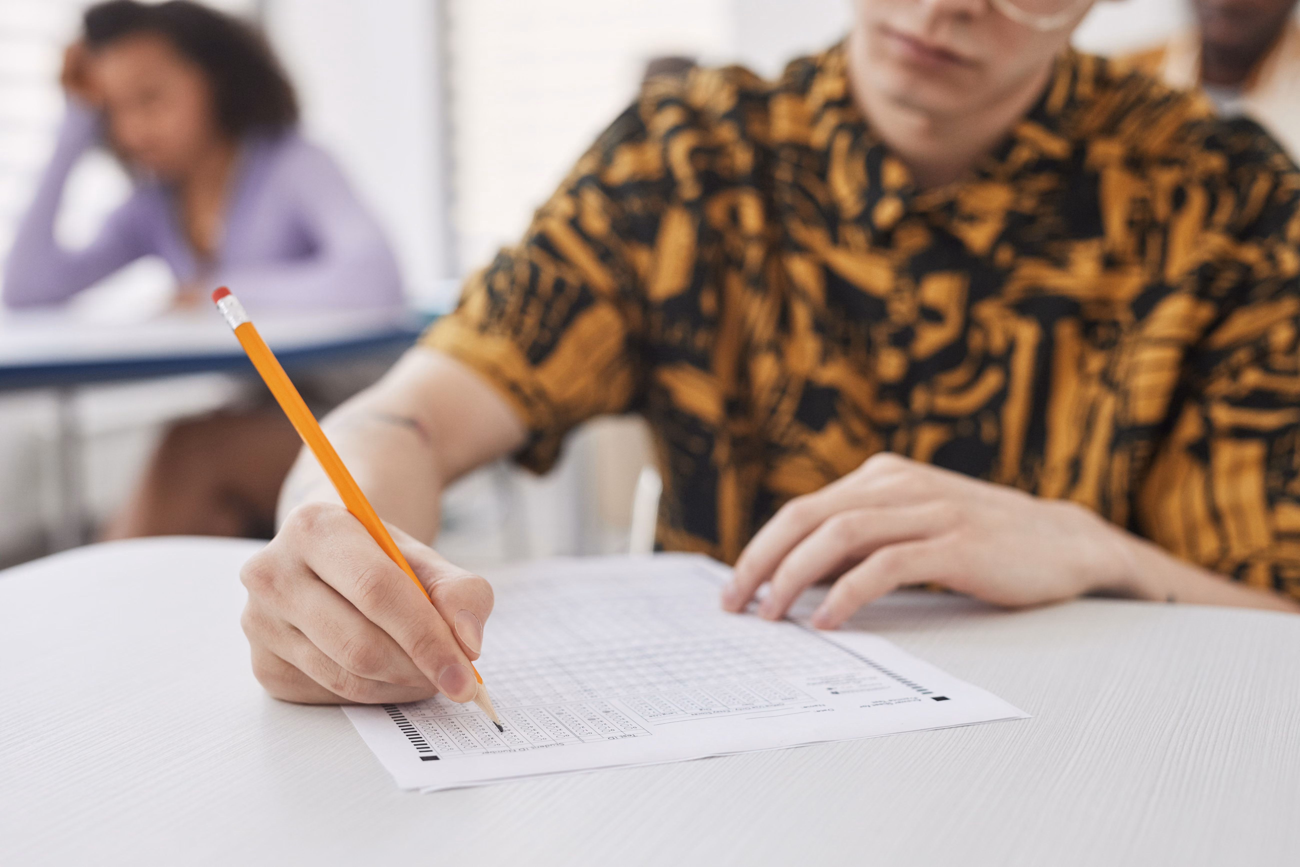 A student's hand writing on exam paper with a pencil during a written examination