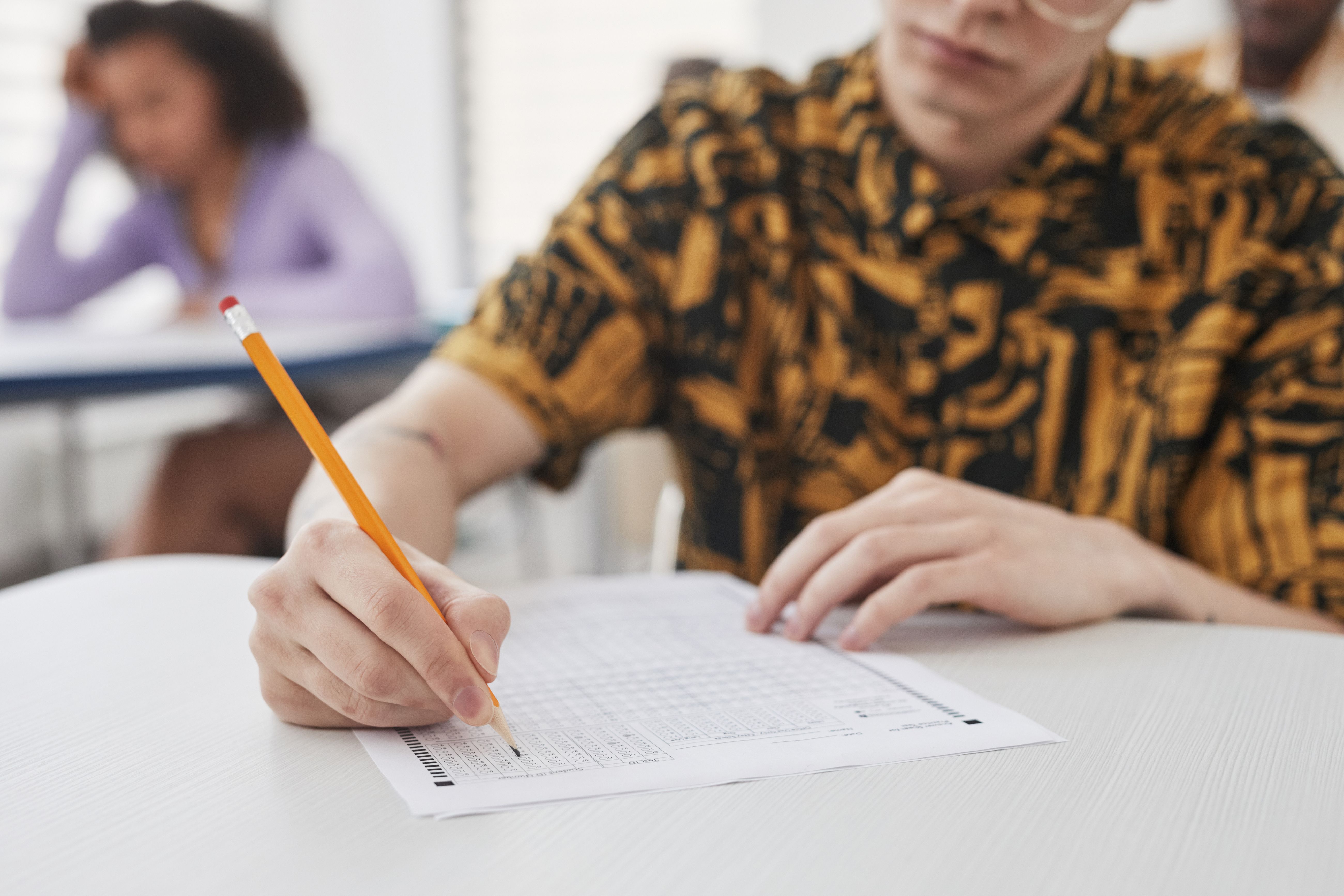 A student's hand writing on exam paper with a pencil during a written examination