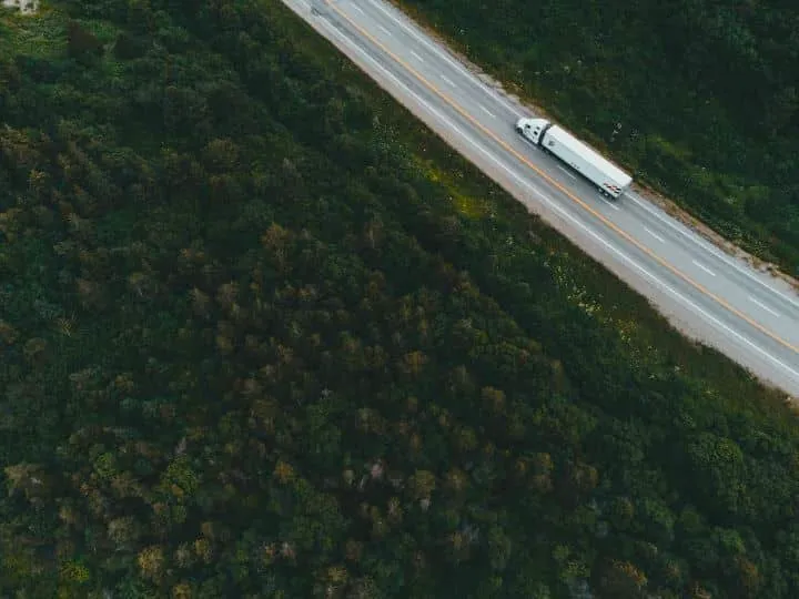 Aerial view of a highway surrounded by forest, showing truck traveling along the road.