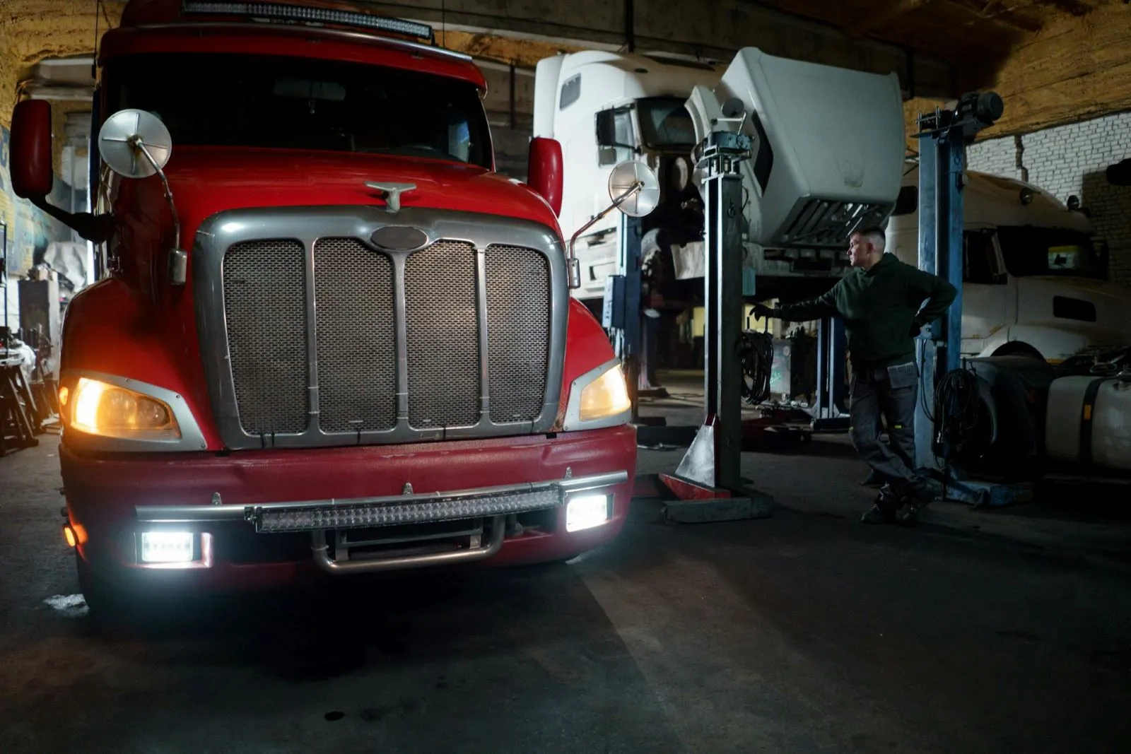 Red fire truck with headlights on parked inside a dim garage
