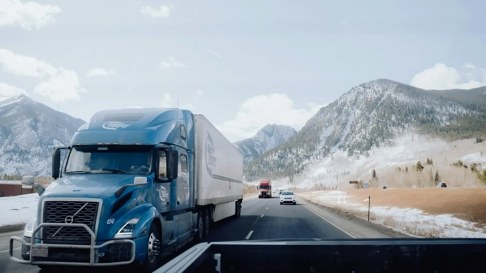 A blue semi-truck travels along a mountain highway