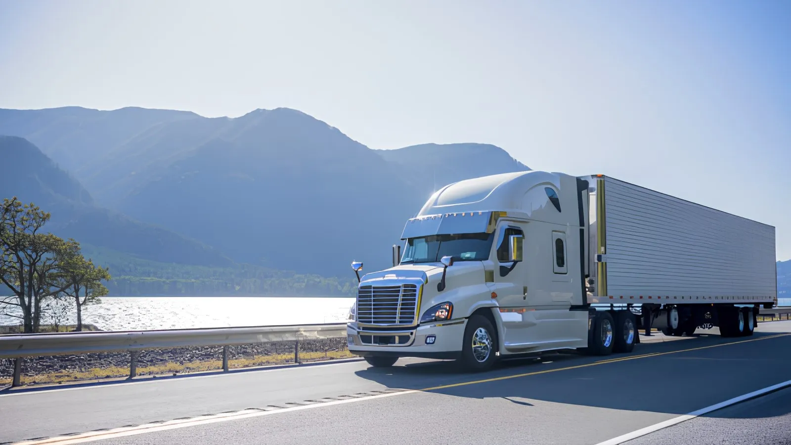 White semi-truck with trailer traveling beside a calm lake and mountains, representing refrigerated freight transport and long-haul reefer trucking.