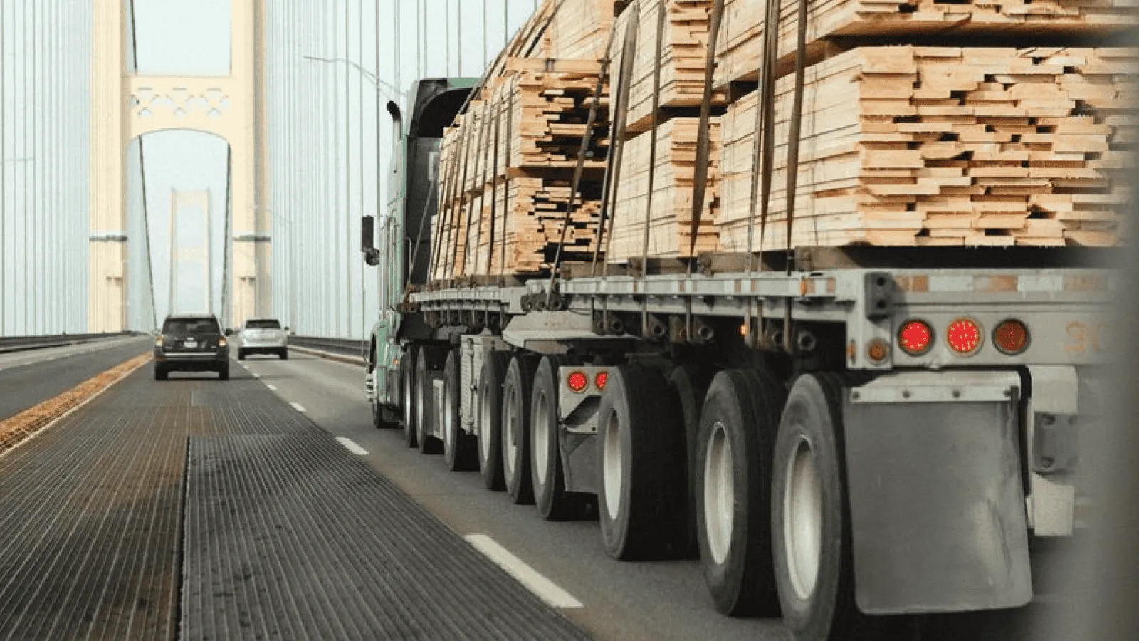 Flatbed semi hauling lumber across a suspension bridge, illustrating one of the key freight truck types.