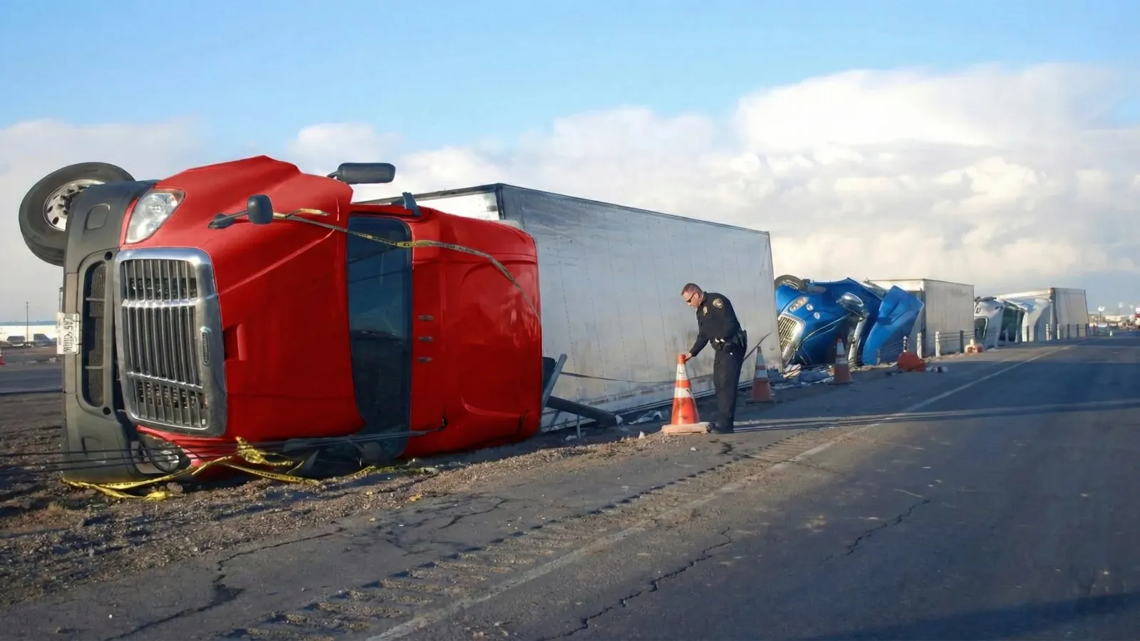 An overturned red semi-truck on a highway illustrates the dangers of trailer sway and loss of control.