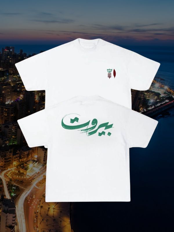 Two white T-shirts with Arabic calligraphy and a green-red logo over Beirut cityscape at dusk.