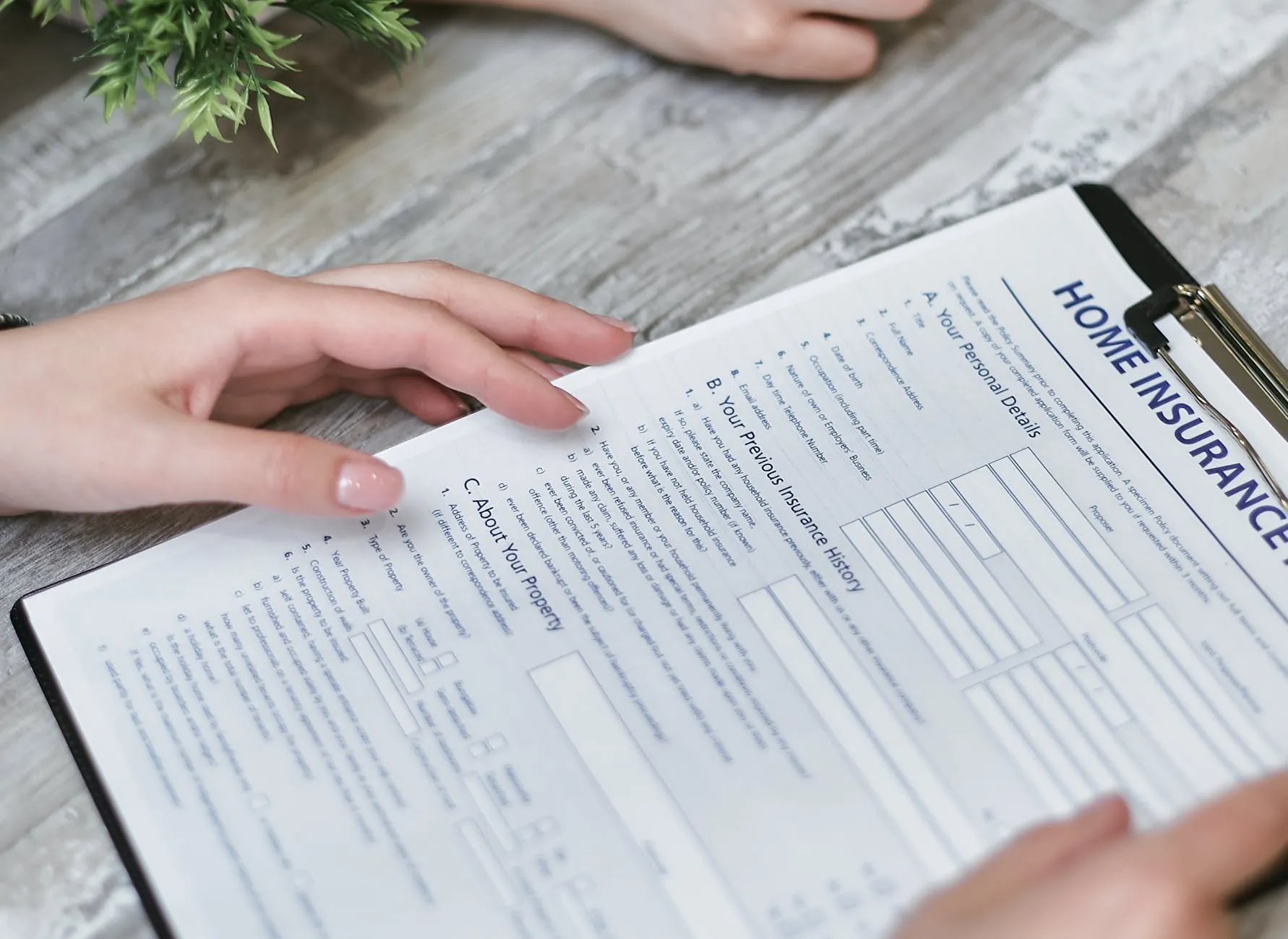 Primer plano de unas manos sosteniendo una carpeta de pinza con un formulario técnico en papel titulado Home Insurance, representando la gestión de un seguro de impago de alquiler