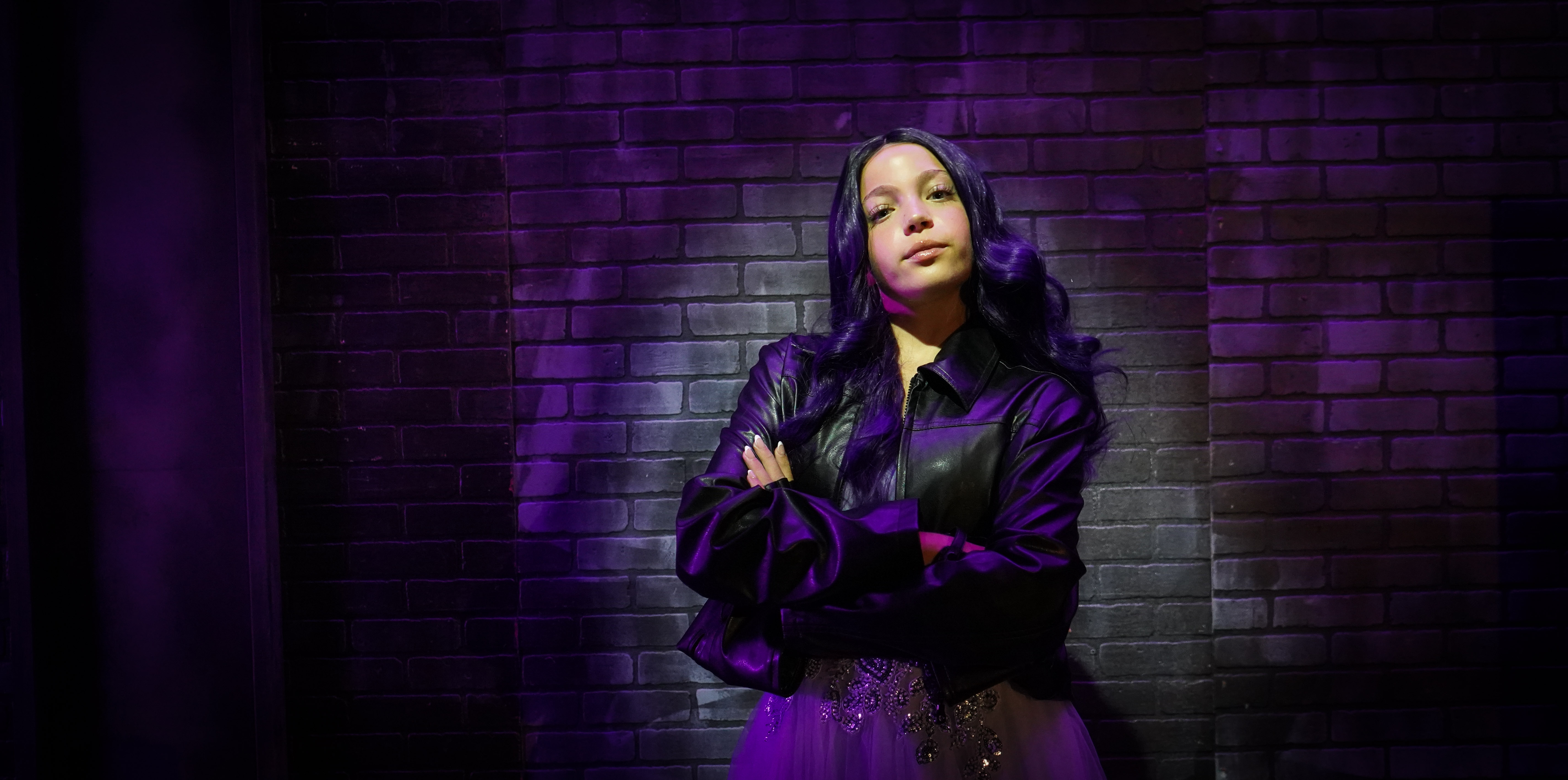 A dramatic shot of Wendesday Addams from behind with purple fog all around
