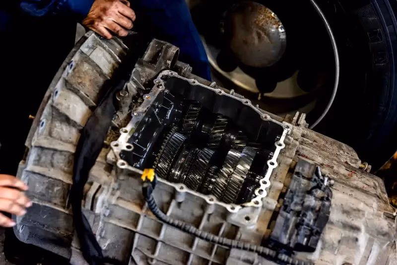 Transmission repair showing exposed gears inside a heavy-duty gearbox with technician’s hands nearby.