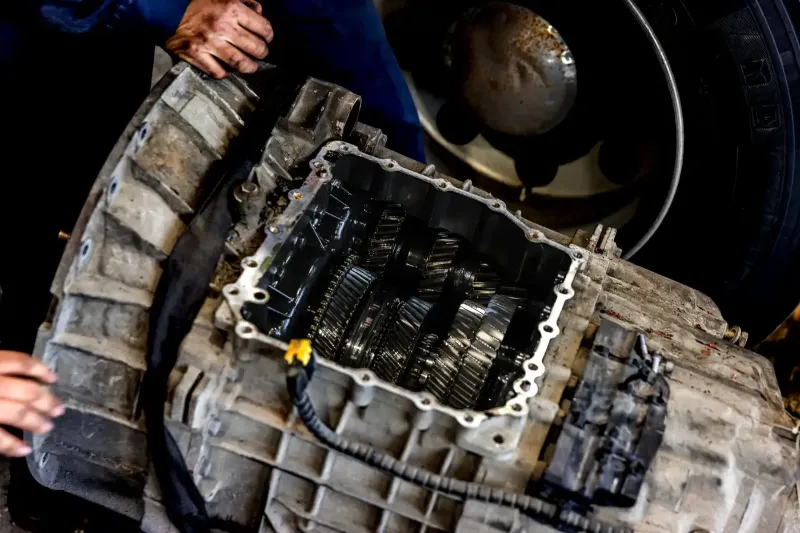 Transmission repair showing exposed gears inside a heavy-duty gearbox with technician’s hands nearby.