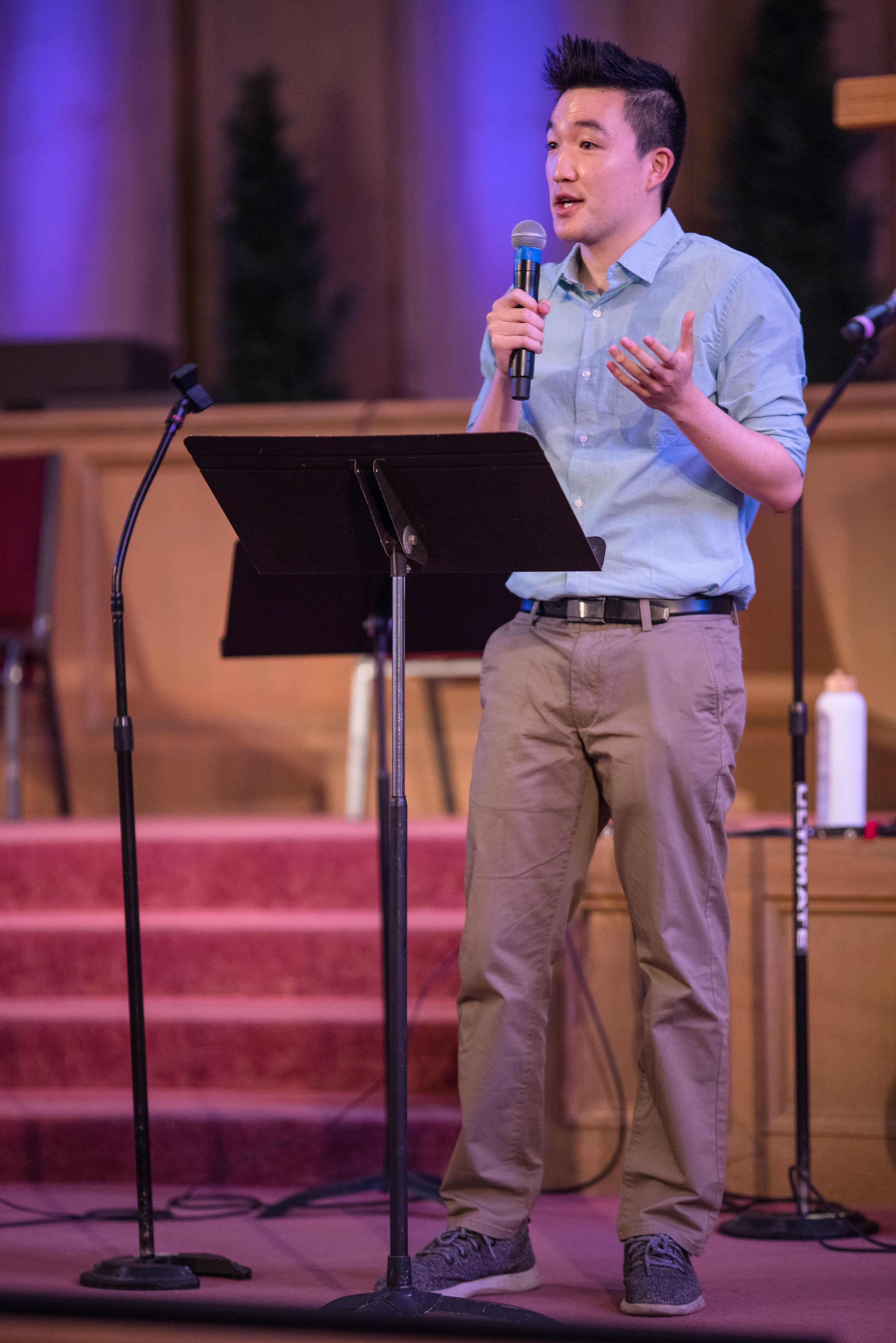 Will speaking into a microphone on stage with a music stand in front of him.