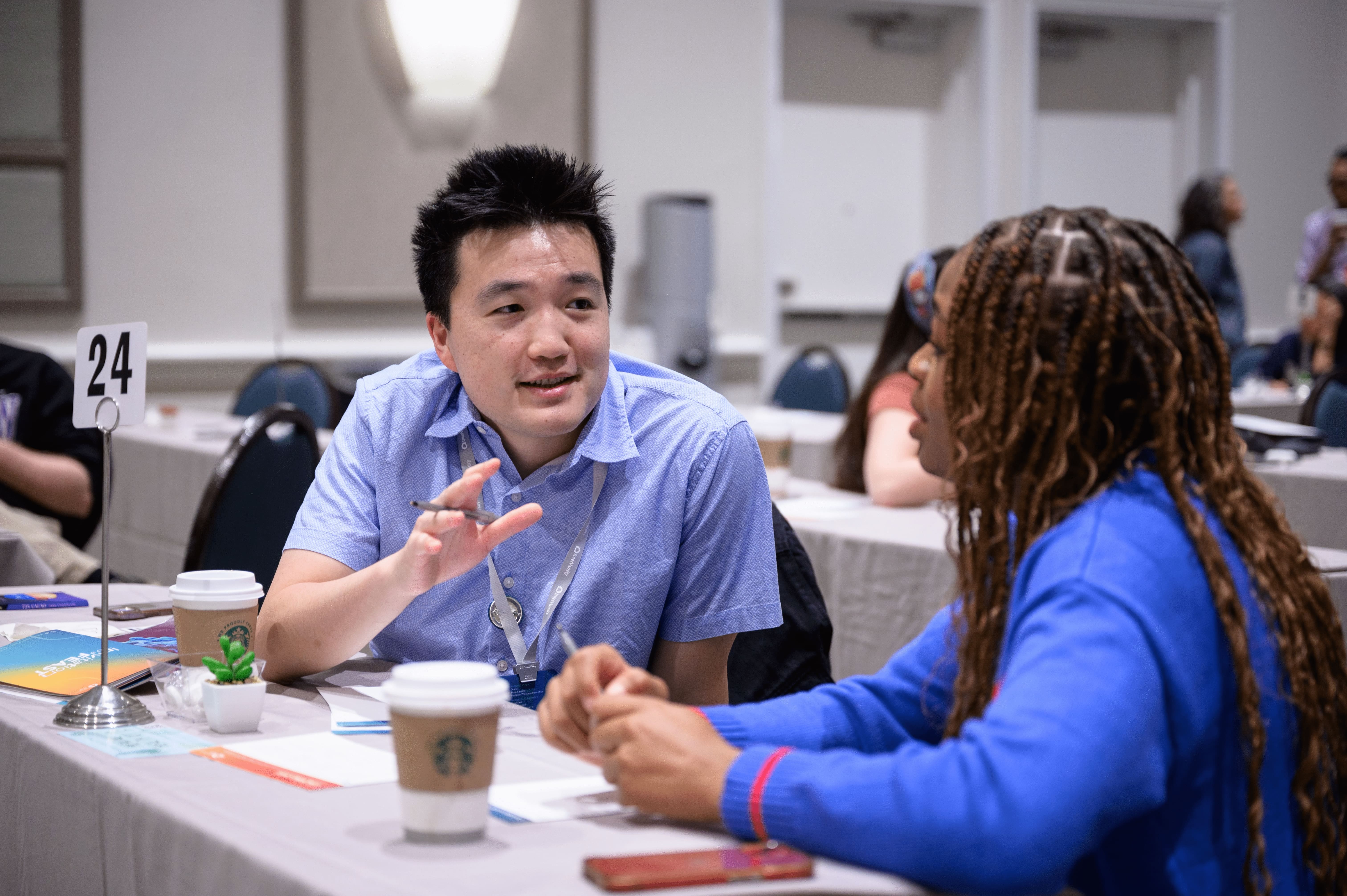 Will engaged in a focused conversation at a conference table with coffee cups and documents.