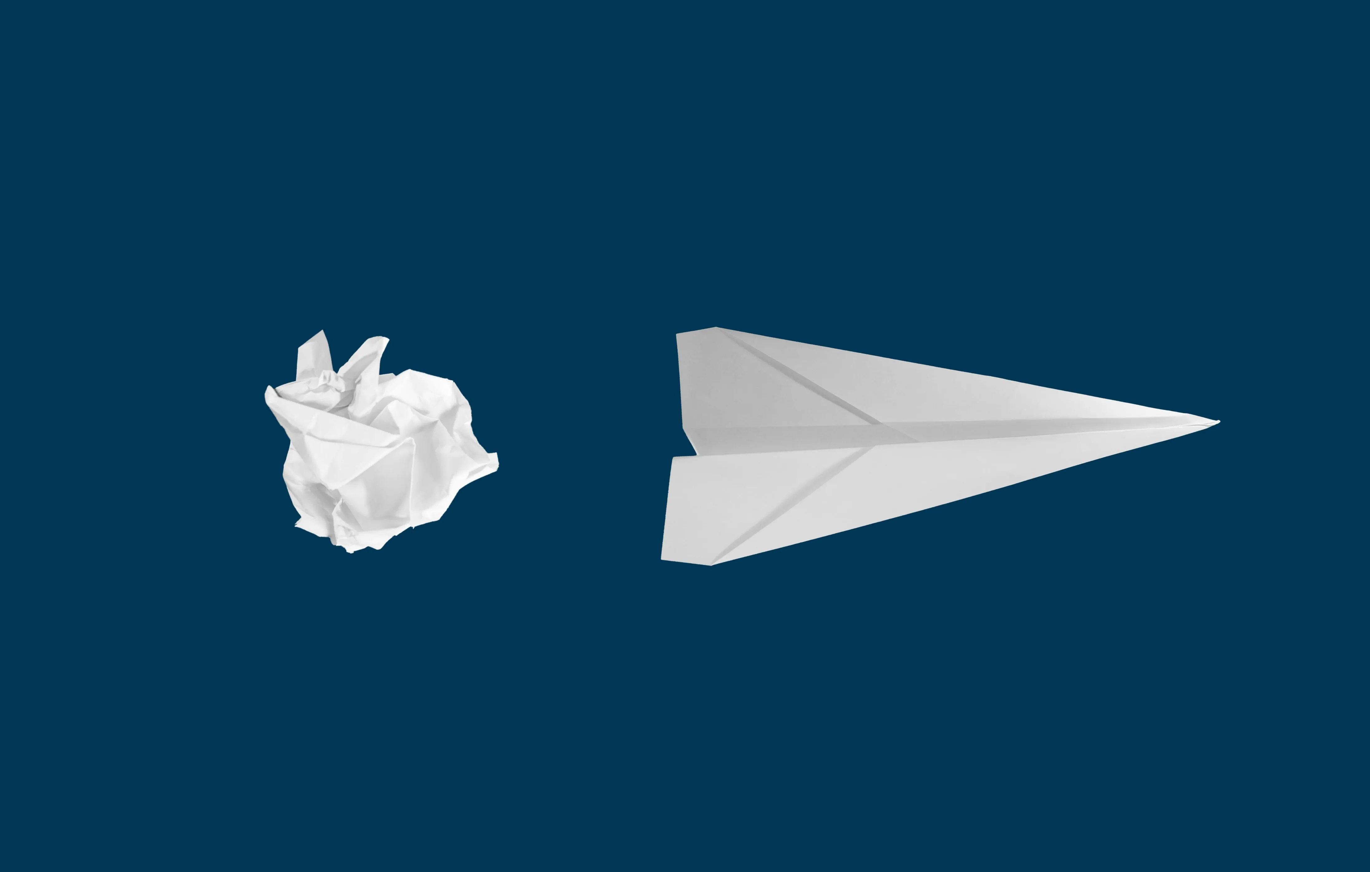 A ball of white paper on the left and a paper plane on the right side of it.