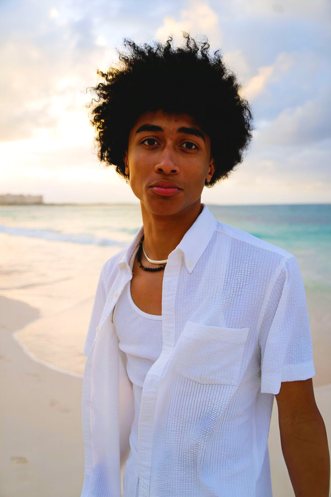 Image of nancy's 18 year old son with brown skin and black hair wearing a white shirt on a beach