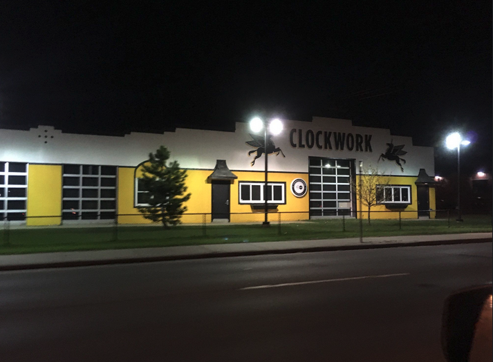 A nighttime photograph of the Clockwork building that is painted yellow, white, and black
