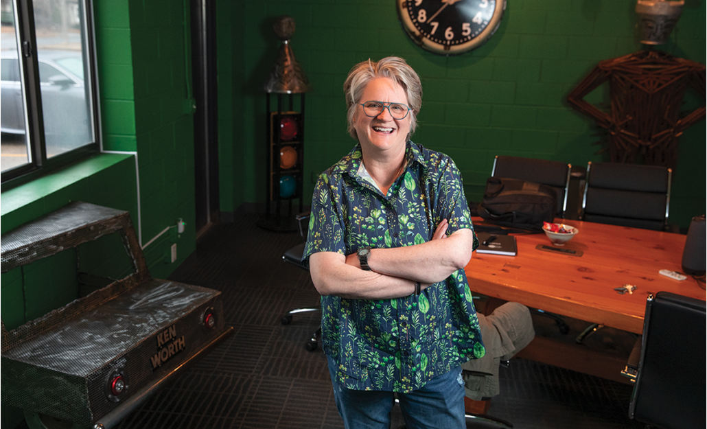 A photo of nancy with folded arms in a green toned button down shirt in front of a conference table