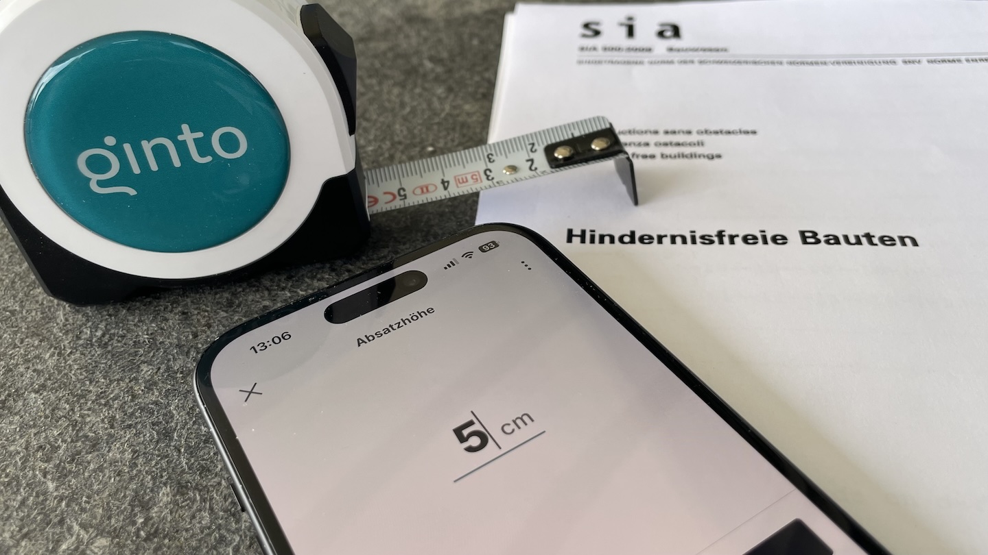 A Ginto tape measure, a mobile phone and the documentation for the SIA 500 standard on ‘Accessible Buildings’ are lying on a table.