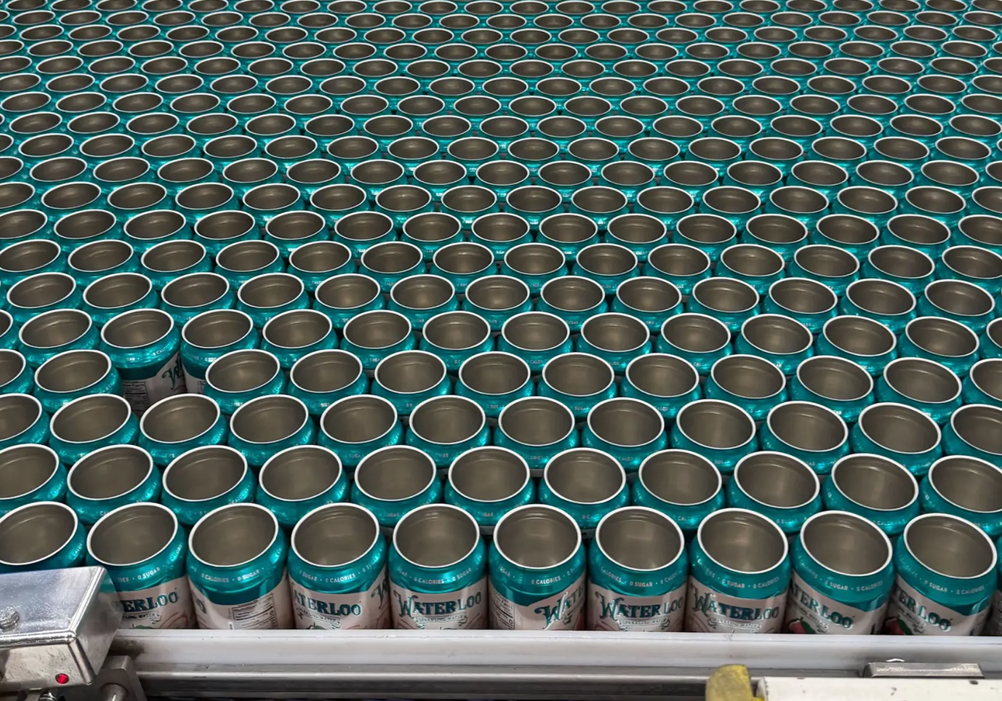 Aluminum cans on the production line all with the same green and white printed label.