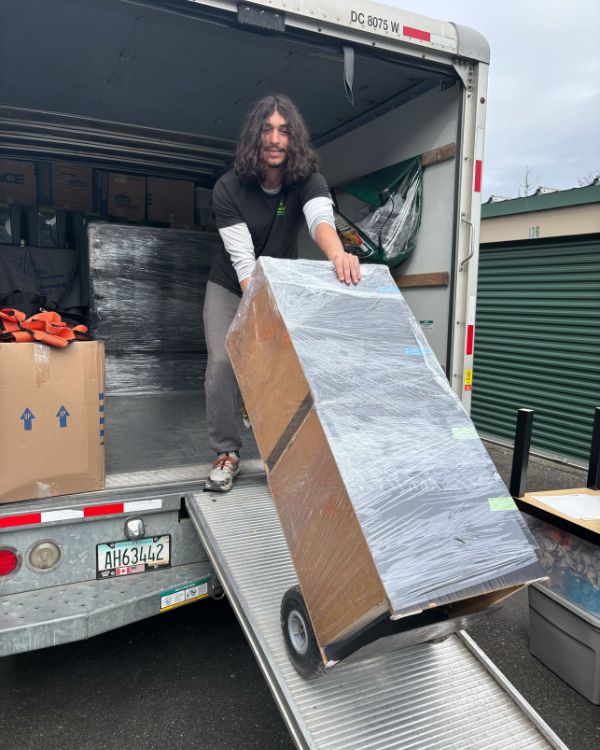 Professional mover unloading furniture with dolly from U-Haul truck during college student apartment move-in.