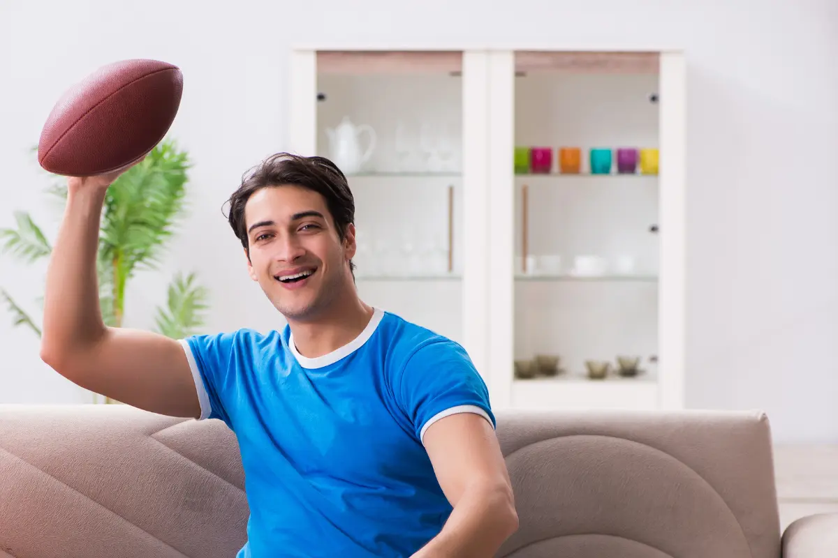 NFL Pick'em pools fan at home holding a football and cheering on his favorite team