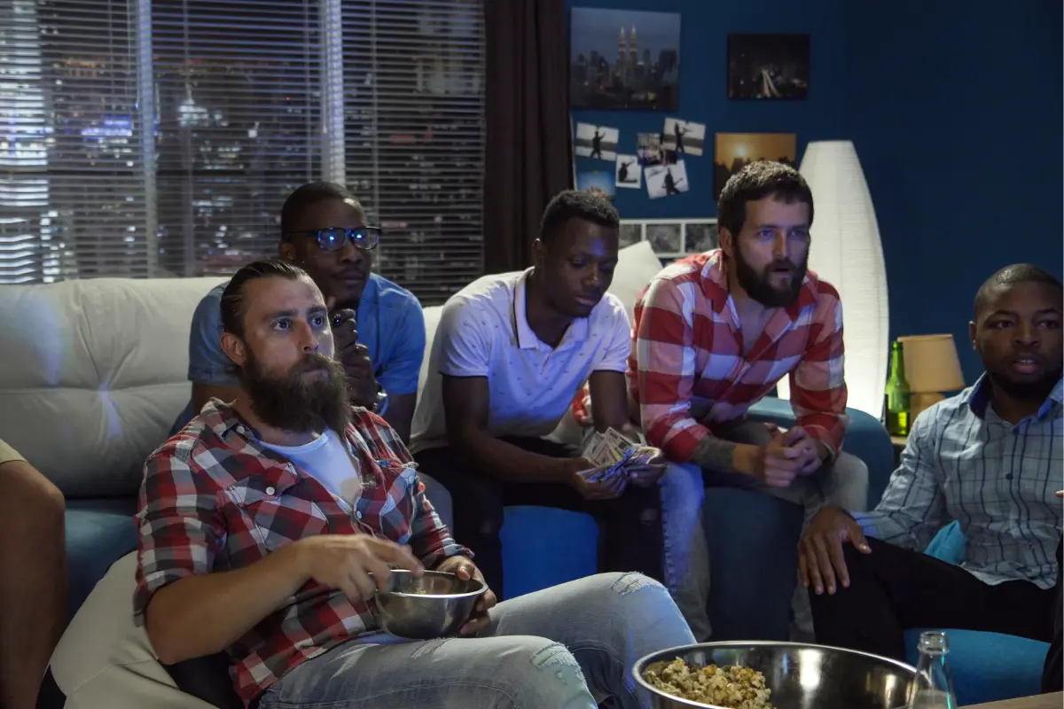Group of men intensely watching a sports game on TV with snacks and drinks in a dimly lit living room