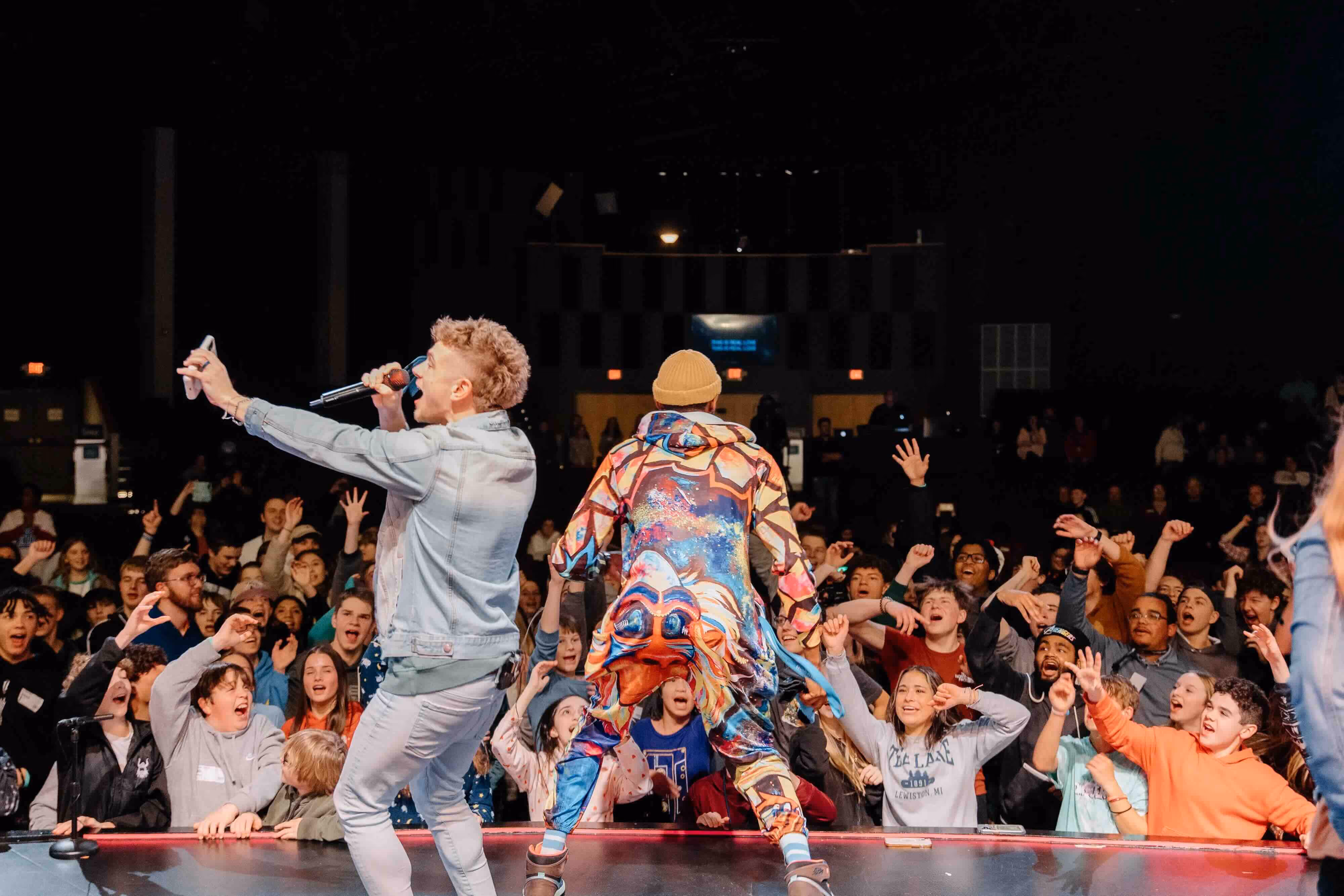 Two performers on stage hyping up a crowd of young people
