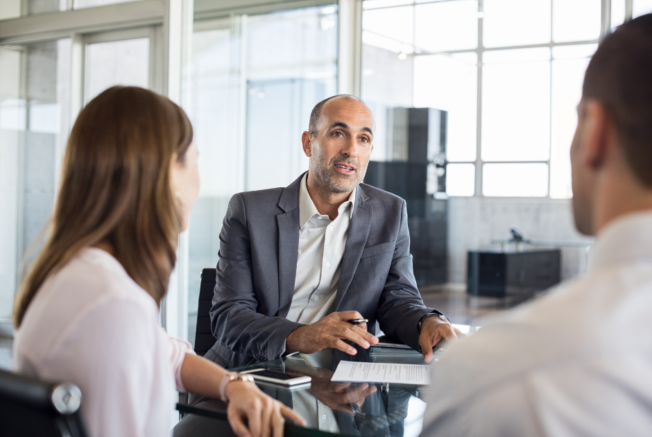 A life insurance advisor sitting with a young couple, smiling during a friendly conversation.