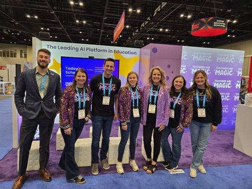 7 MagicSchool employees in branded clothing posing for group photo in front of MagicSchool's booth at a conference