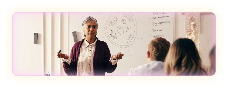 Female teacher standing in front of a whiteboard in a classroom with students at the desks in front of her. 