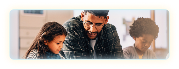 Male teacher sitting between two students helping them in a classroom setting.