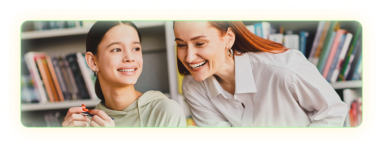 Smiling female teacher leaning over a smiling student's desk to view her work. 
