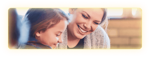 Female teacher smiling and leaning down next to a young student to help her.