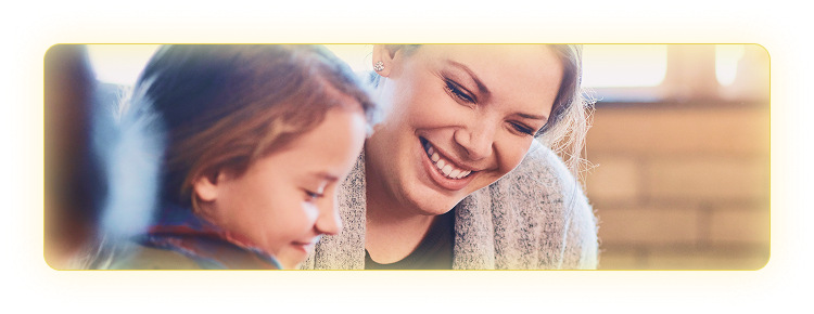 Female teacher smiling and leaning down next to a young student to help her.