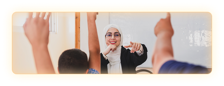 Female teacher in front a classroom with students at their desks with their hands raised. 