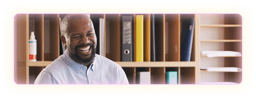 Male teacher in white button up shirt smiling in a classroom setting.