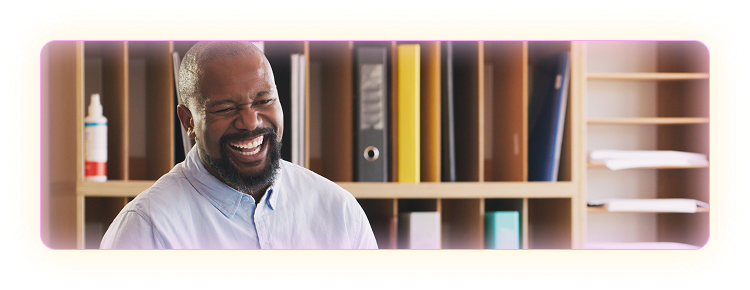 Male teacher in white button up shirt smiling in a classroom setting.