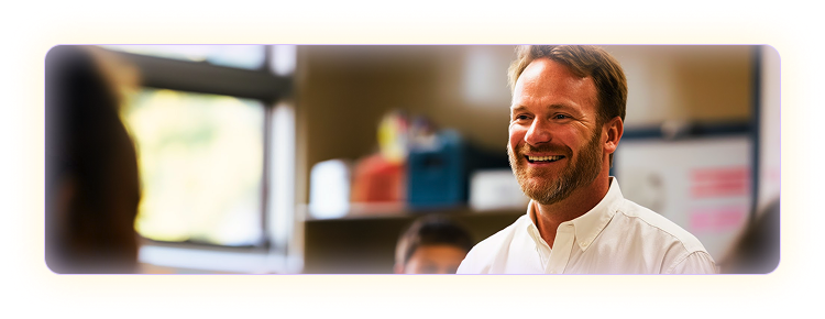 Male teacher in white button up shirt smiling in a classroom setting.