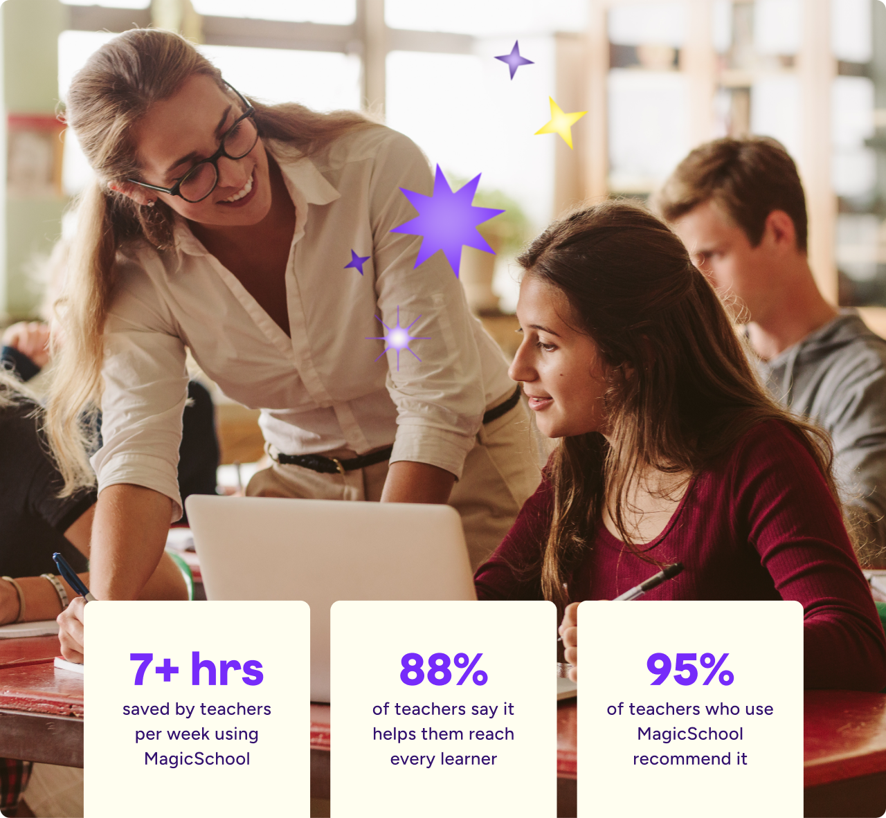 A teacher leans over a student’s desk, smiling as they look at a laptop together in a classroom. Other students work in the background