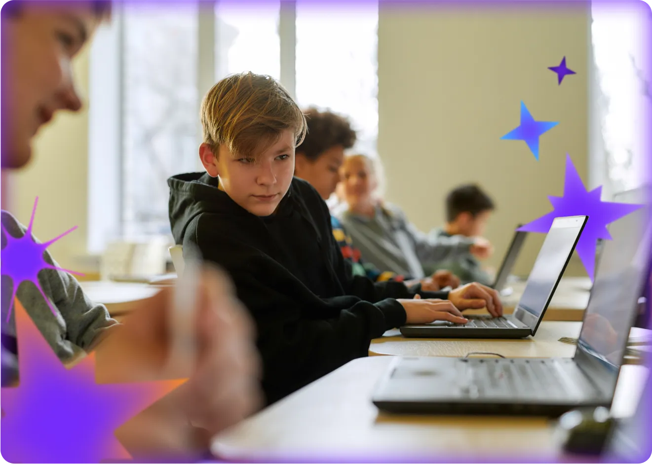 Middle school student using a laptop in a classroom, with other students working on laptops in the background.