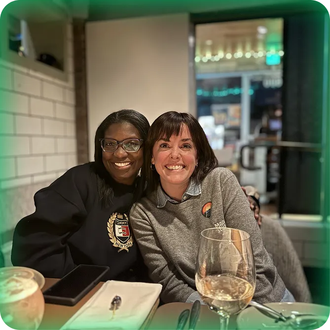 2 MagicSchool employees sitting together and smiling at a restaurant.