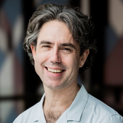 Headshot of Chris Rohlfs wearing a light green collared shirt, standing in front of a softly blurred indoor background.