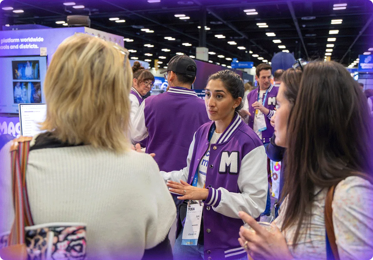 MagicSchool employee wearing a purple, branded letterman's jacket and speaking with educators at a trade show