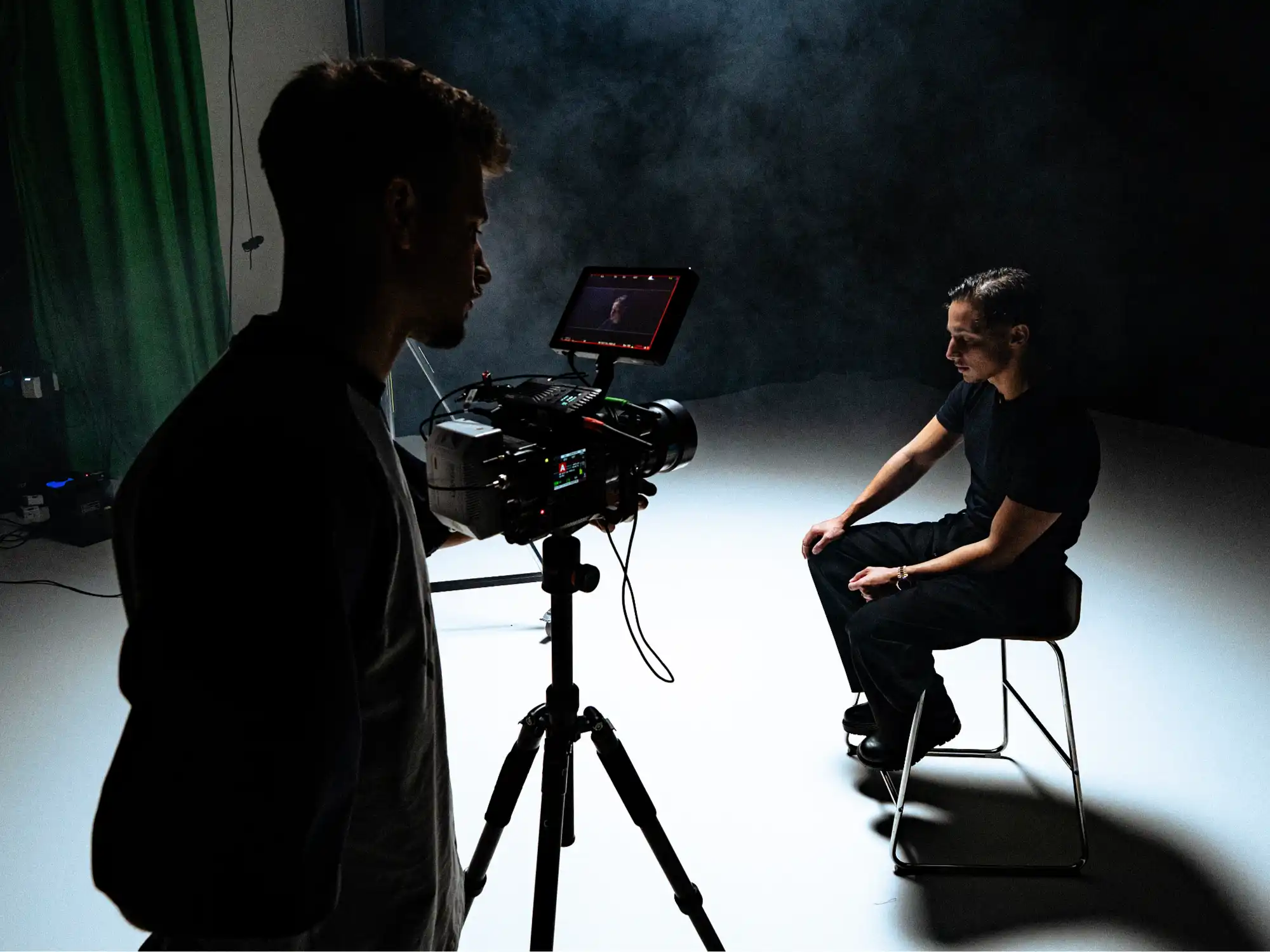 Kamera auf Stativ und sitzende Person im beleuchteten Studio beim Musikvideodreh zu „Deine Liebe“.