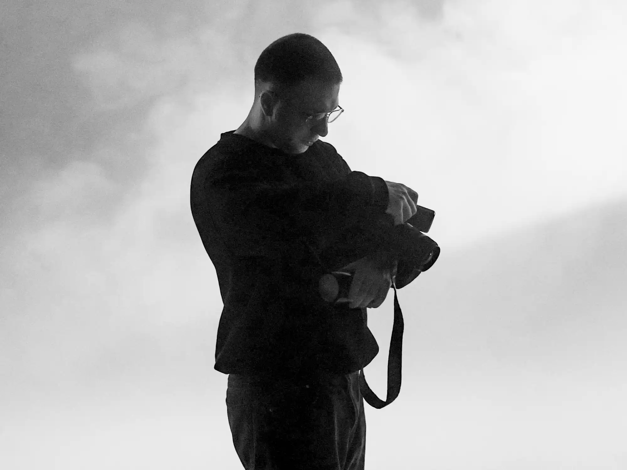 Alexander Gorszczynski als Silhouette vor hellem, nebligem Studiohintergrund mit Kamera in der Hand.