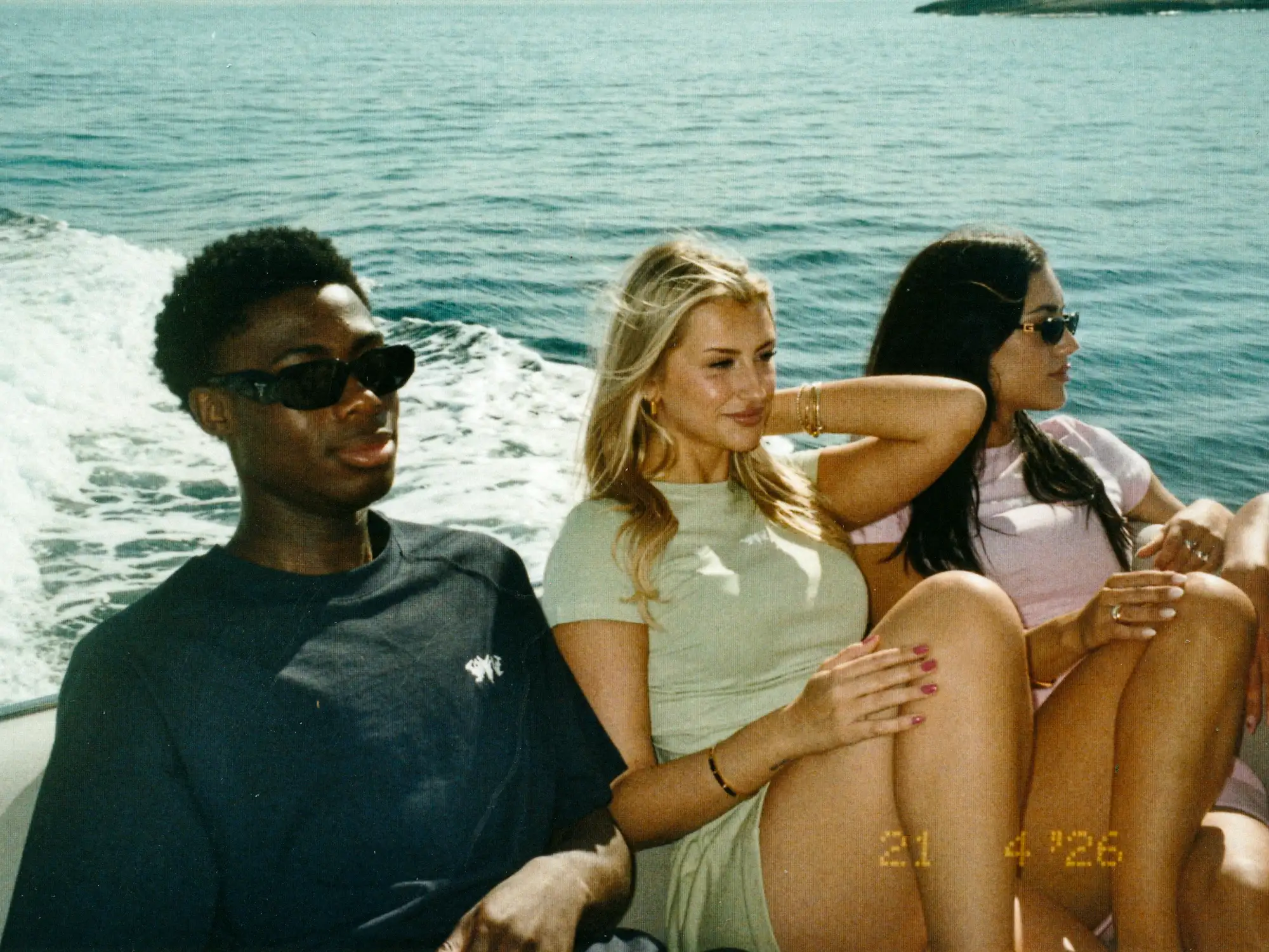 Drei Models sitzen gemeinsam auf dem Yachtdeck, mit dem Meer im Hintergrund.